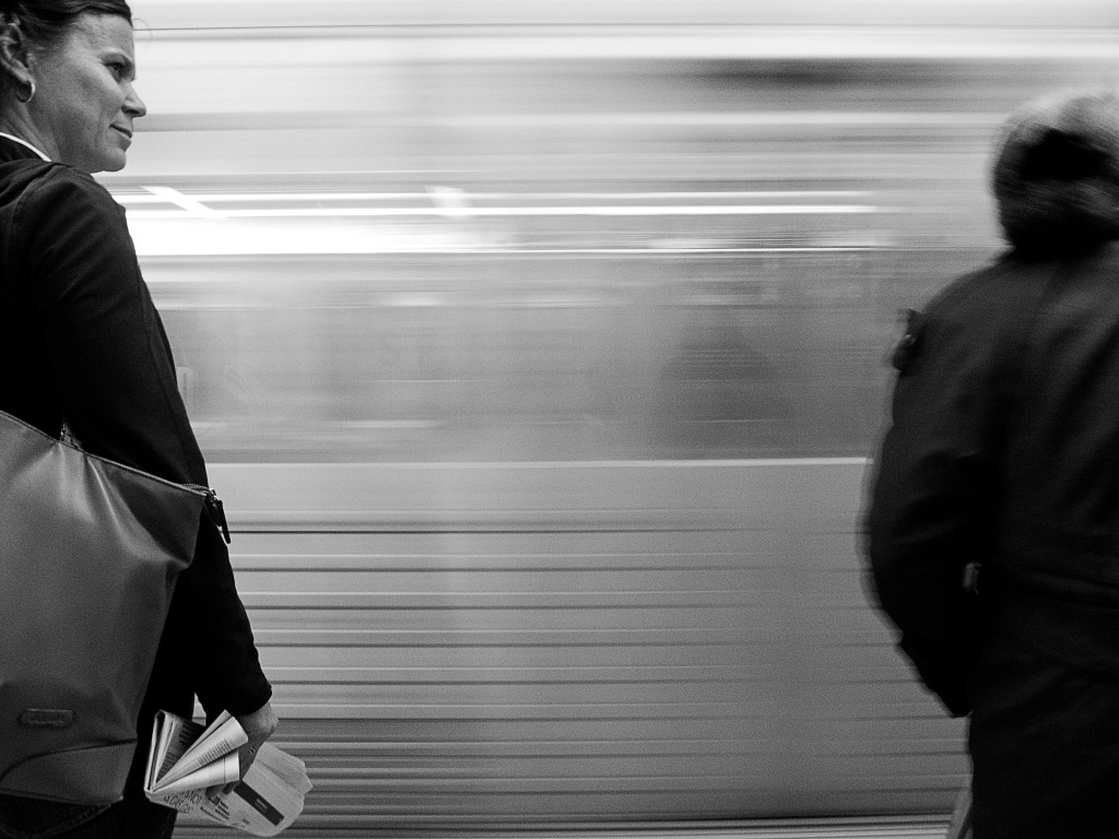 woman looks down subway platform as subway train speeds behind her